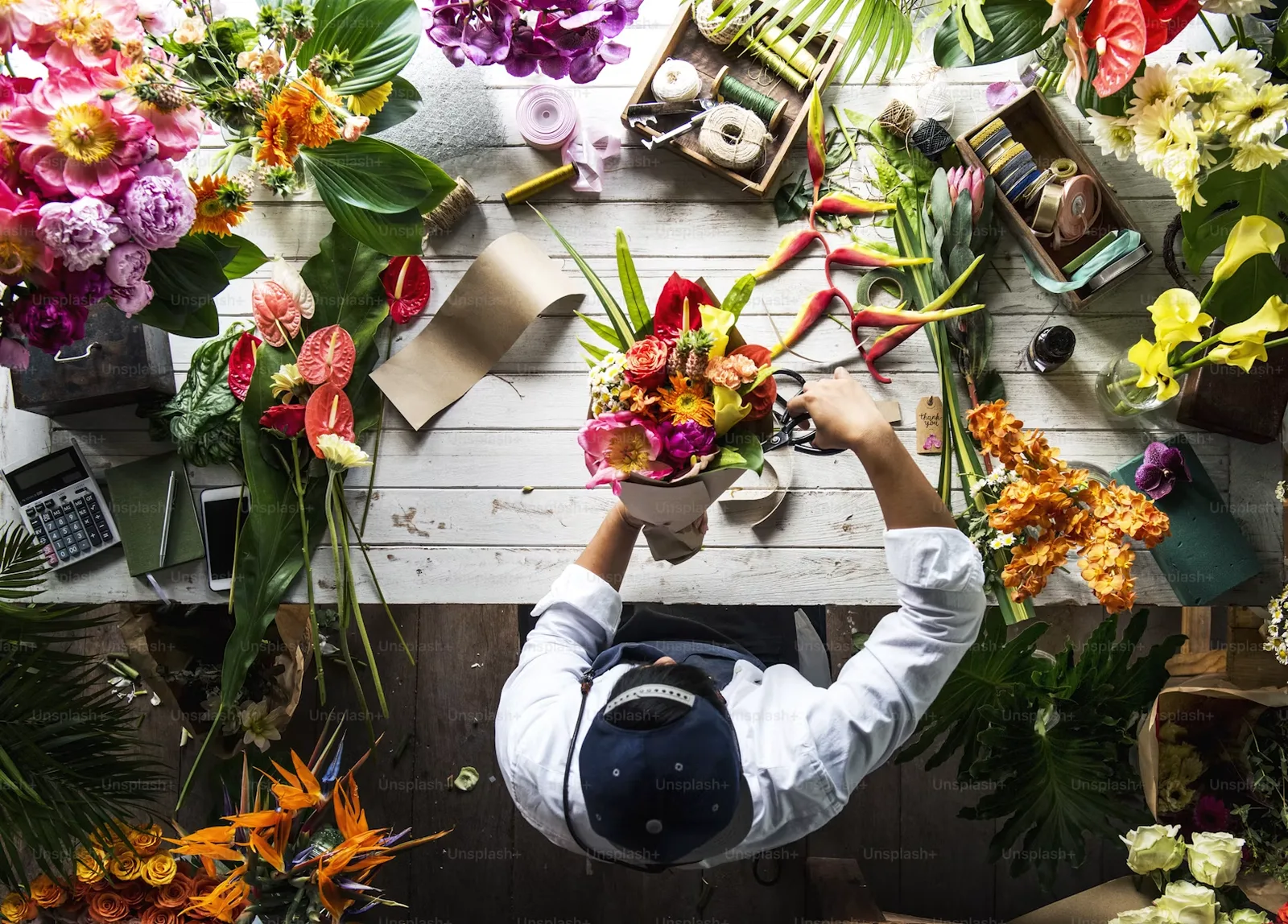 Florist assembling a bouquet among flowers, tools, and packaging materials in a busy studio
