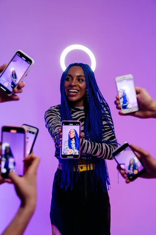 A human fashion influencer with blue braids surrounded by phones in a purple studio.